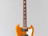 an orange electric guitar hanging from a string on a white wall