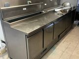 un plan de travail en acier inoxydable dans la cuisine d'un restaurant, avec un panneau affichant le menu accroché au mur