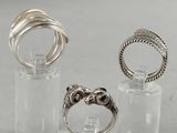 trois bagues différentes dans un support en verre transparent posé sur une surface blanche