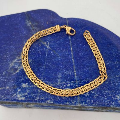a close up of a gold chain bracelet on a blue stone