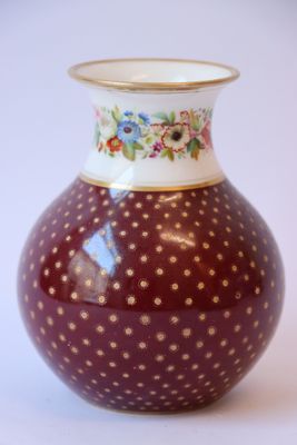 un vase rouge parsemé de points dorés sur un fond blanc