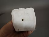 a hand holding a piece of white marble with a hole in it