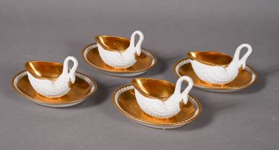 four gold and white porcelain swan cups and saucers on a plate