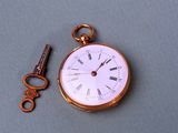 a gold pocket watch and a key on a table
