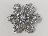 a close up of a diamond flower brooch on a white surface