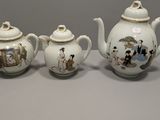 three porcelain teapots and a teapot with a picture of people on them
