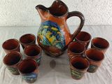 six cups and a pitcher on a table with a white cloth