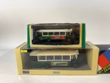 two green and white model buses in boxes on a white surface