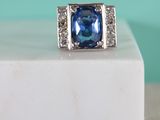 une photo d'une bague sertie d'un saphir bleu et de diamants, posée sur un bloc de marbre blanc