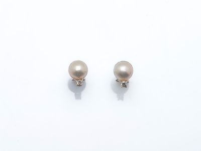 une paire de boucles d'oreilles en perles et diamants posées sur une surface blanche
