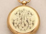 a gold pocket watch with a monogram on it