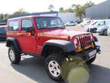 a red jeep parked in a parking lot with other cars in the background