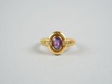 gros plan d'une bague en or avec une pierre violette