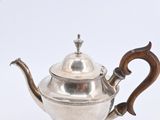 an antique silver teapot with a wooden handle on a white surface
