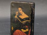 une vieille boîte noire sur laquelle est peinte une femme assise sur une chaise