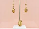 a pair of gold earrings on a stand against a pink wall
