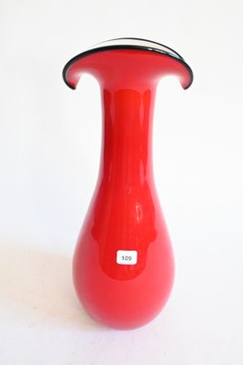 un vase rouge bordé de noir posé sur une surface blanche