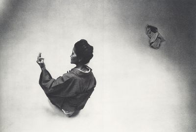black and white photograph of a woman sitting on the ground with a butterfly in her hand