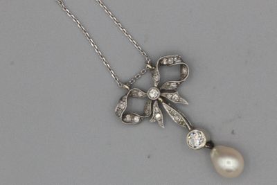 une photo d'un pendentif en forme de nœud, orné d'une perle et d'un diamant, monté sur une chaîne