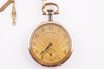 une montre de poche en or avec une chaîne, posée sur une surface blanche