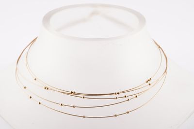 trois colliers en or sur un mannequin blanc coiffé d'un chapeau blanc