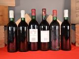 six bottles of red wine are lined up on a table