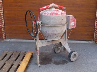 une bétonnière posée sur une palette devant la porte d'un garage
