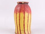 un vase rouge et jaune posé sur une surface blanche