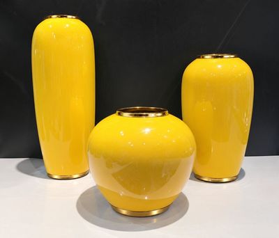 three yellow vases sitting on a white table with a black background