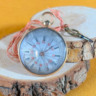 a silver pocket watch on a piece of wood on a yellow background