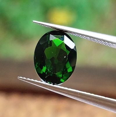 someone holding a pair of pliers with a green tourmaline gemstone