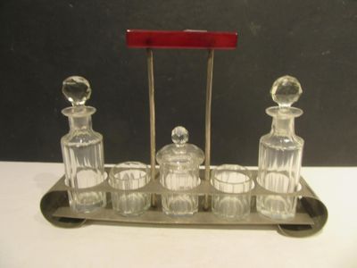 un plateau en argent avec quatre carafes en verre et une poignée rouge