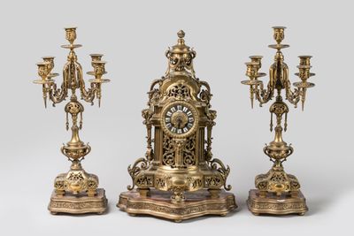 trois bougeoirs dorés et une horloge posés sur une table