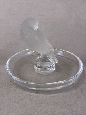 un oiseau en verre posé sur une assiette en verre posée sur une table