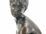 bronze statue of a boy sitting on a rock with his hands on his knees