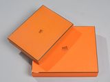 une boîte orange, dont le couvercle est ouvert, posée sur une surface blanche