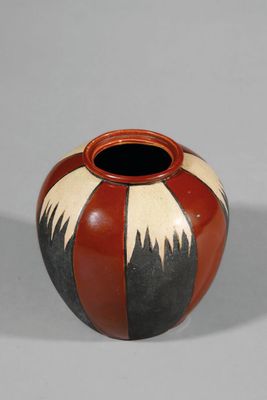 un vase rouge et noir posé sur une surface blanche