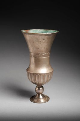 an old silver vase sitting on top of a table next to a gray wall