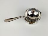 a silver strainer with a spoon on a white surface