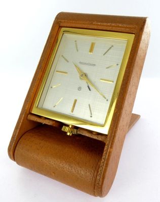 une petite horloge en bois posée sur un socle, sur une surface blanche