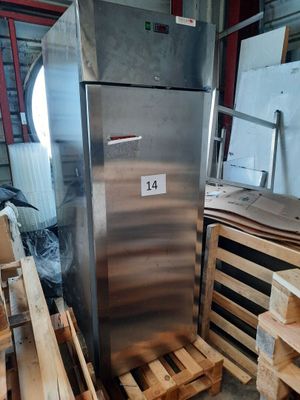 un réfrigérateur argenté posé dans un entrepôt, entouré de palettes en bois