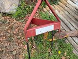 une charrue rouge posée dans l'herbe à côté d'un tas de bois