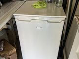 a small white refrigerator in a kitchen with a lot of clutter on the counter