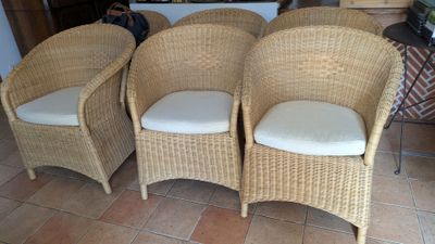 Trois fauteuils en osier avec des coussins sont disposés sur le carrelage du salon.