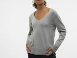 a woman wearing a grey sweater and black pants stands in front of a white wall
