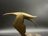 sculpture représentant un oiseau volant au-dessus d'une pièce de monnaie posée sur une surface grise