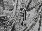 photographie en noir et blanc d'un homme portant un chapeau et un manteau, debout dans les bois