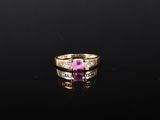 une bague sertie d'un saphir rose et de diamants, posée sur un fond noir