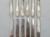 six silverplated knives and six knives on a white surface