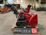 une déneigeuse rouge posée sur une palette dans un entrepôt